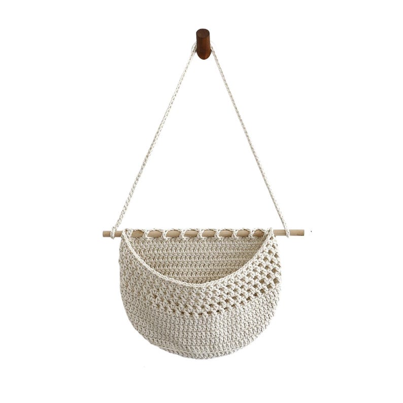 Puede incluir: Una cesta colgante de macram&eacute; de color crema, con una clavija de madera y una clavija de madera marr&oacute;n oscuro para colgarla. La cesta tiene forma semicircular con un dise&ntilde;o tejido. Se suspende con una cuerda de color crema.