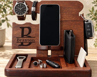 May include: A dark brown wooden docking station featuring a personalized engraving of the letter B and the name Braxton. The organizer includes slots for a smartphone, a wristwatch, a bracelet, a wallet, keys, cufflinks, a ring, and a tool.