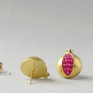 May include: A pair of gold earrings shaped like pomegranates. The earrings are open and filled with small red gemstones.