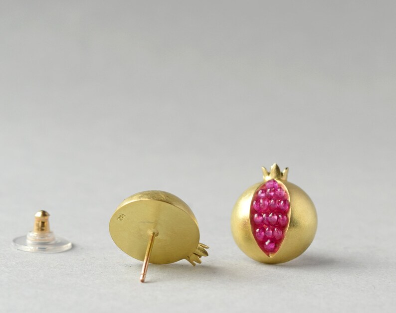 May include: A pair of gold earrings shaped like pomegranates. The earrings are open and filled with small red gemstones.
