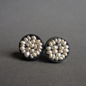 May include: A pair of black stud earrings with a circular design made of small white pearls.