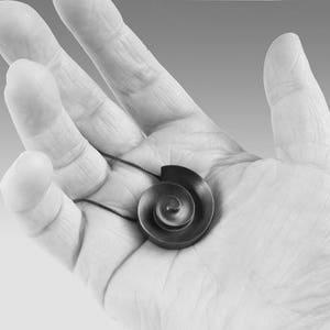 Pu&ograve; includere: Una collana con un ciondolo d'argento a forma di spirale. Il ciondolo &egrave; tenuto in una mano.
