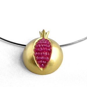 Pu&ograve; includere: Una collana d'oro con un ciondolo a forma di melograno. Il ciondolo &egrave; aperto per rivelare un gruppo di pietre di rubino rosa.