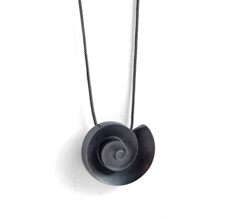 Pu&ograve; includere: Una collana in metallo nero con un ciondolo a spirale. Il ciondolo &egrave; composto da due pezzi di metallo uniti per formare una forma a spirale.