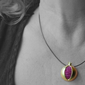 Pu&ograve; includere: Una collana d'oro con un ciondolo a forma di melograno. Il ciondolo &egrave; in oro e ha un centro di rubino rosso.