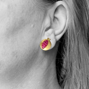 May include: A pair of gold earrings shaped like pomegranates with red ruby stones.