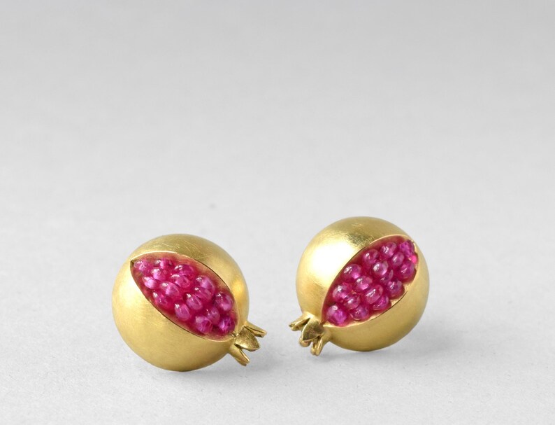 May include: A pair of gold earrings shaped like pomegranates, each with a section cut out to reveal a cluster of pink gemstones.