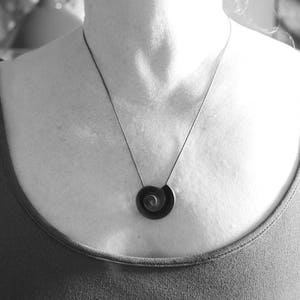 Pu&ograve; includere: Una collana nera e argentata con un ciondolo a spirale.