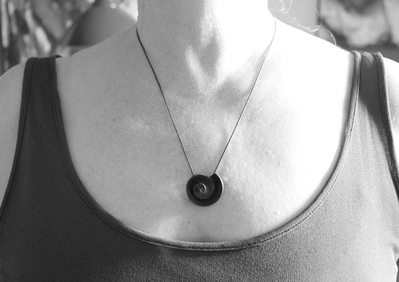 Pu&ograve; includere: Una collana nera e argentata con un ciondolo a spirale.