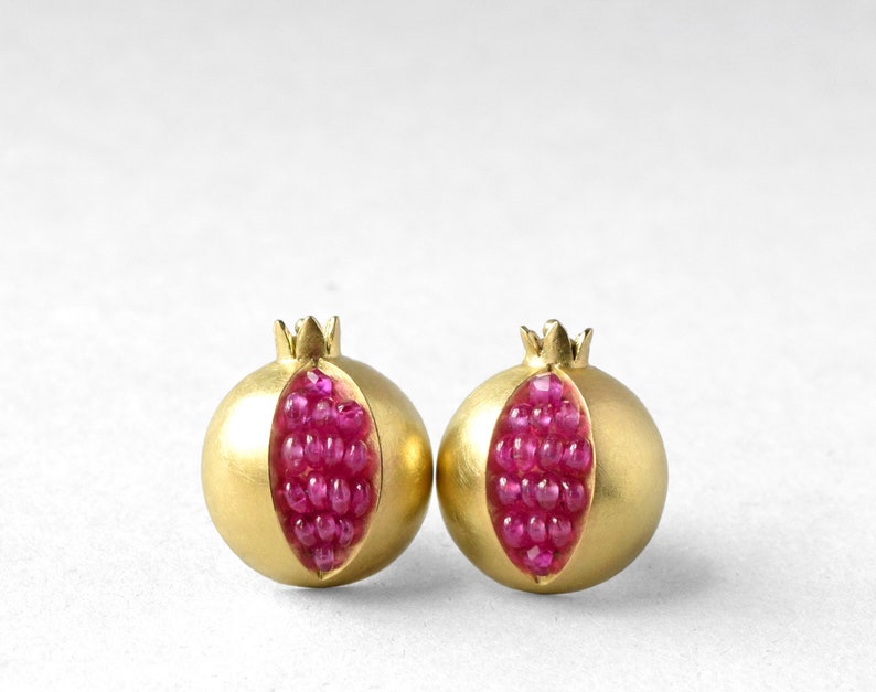 May include: A pair of gold earrings shaped like pomegranates, each with a red ruby gemstone centre.