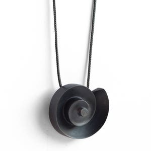 Pu&ograve; includere: Una collana con un ciondolo in argento ossidato nero a forma di spirale. Il ciondolo &egrave; sospeso da un cordoncino nero.