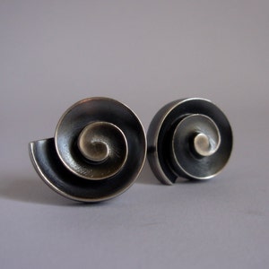 May include: A pair of silver earrings with a spiral design. The earrings are made of metal and have a dark, oxidized finish.