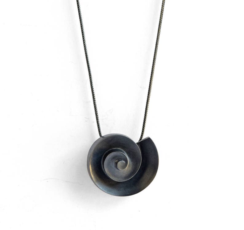 Pu&ograve; includere: Una collana d'argento con un ciondolo nero a forma di spirale. Il ciondolo &egrave; composto da due pezzi di metallo uniti per formare una spirale.