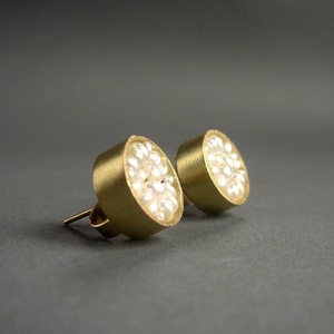 May include: A pair of gold-colored stud earrings. Each earring features a circular design filled with small, white pearls. The earrings have a post and backing for secure wear. The background is a solid, dark gray.