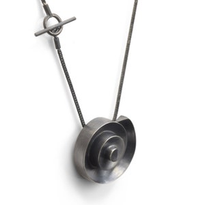 Pu&ograve; includere: Una collana d'argento con un ciondolo a spirale. Il ciondolo &egrave; realizzato con pi&ugrave; strati di metallo, creando un effetto tridimensionale.