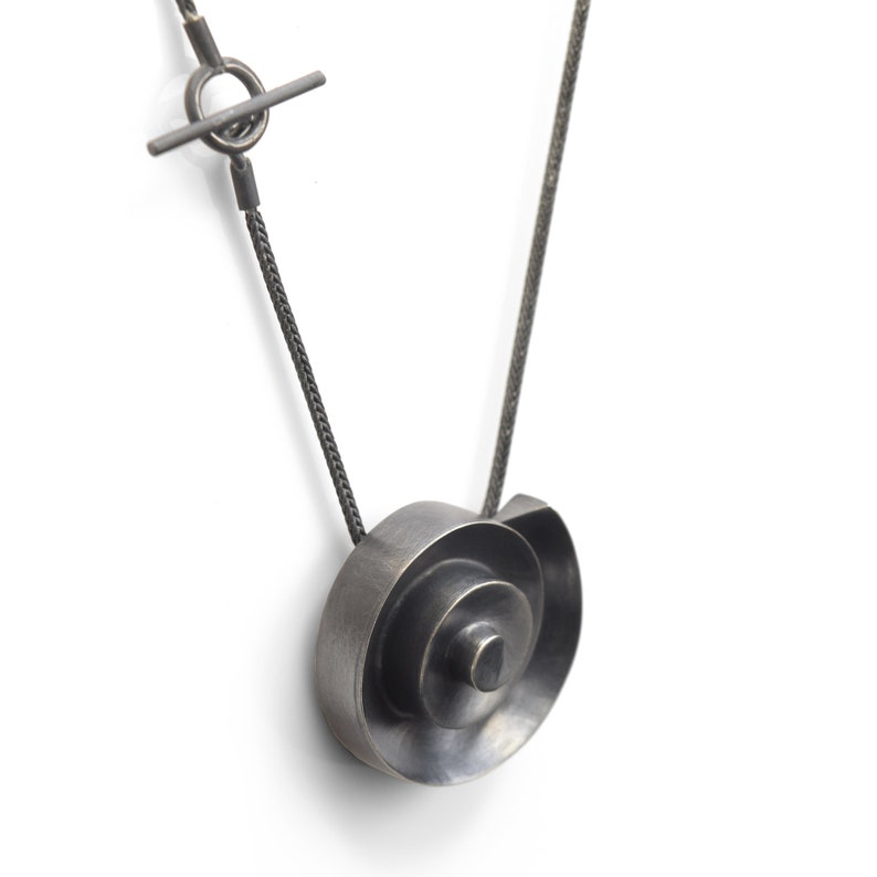Pu&ograve; includere: Una collana d'argento con un ciondolo a spirale. Il ciondolo &egrave; realizzato con pi&ugrave; strati di metallo, creando un effetto tridimensionale.