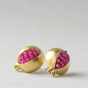 May include: A pair of gold earrings shaped like pomegranates, each with a cluster of pink gemstones inside.