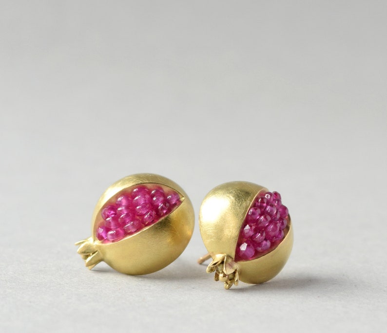 May include: A pair of gold earrings shaped like pomegranates, each with a cluster of pink gemstones inside.