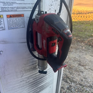 Może przedstawiać: Czerwono-czarne narzędzie elektryczne Milwaukee, prawdopodobnie wiertarka lub zakrętarka udarowa, jest zamontowane na białej powierzchni. Narzędzie ma czarny uchwyt i srebrny osprzęt. Czarny kabel jest owinięty wok&oacute;ł narzędzia.
