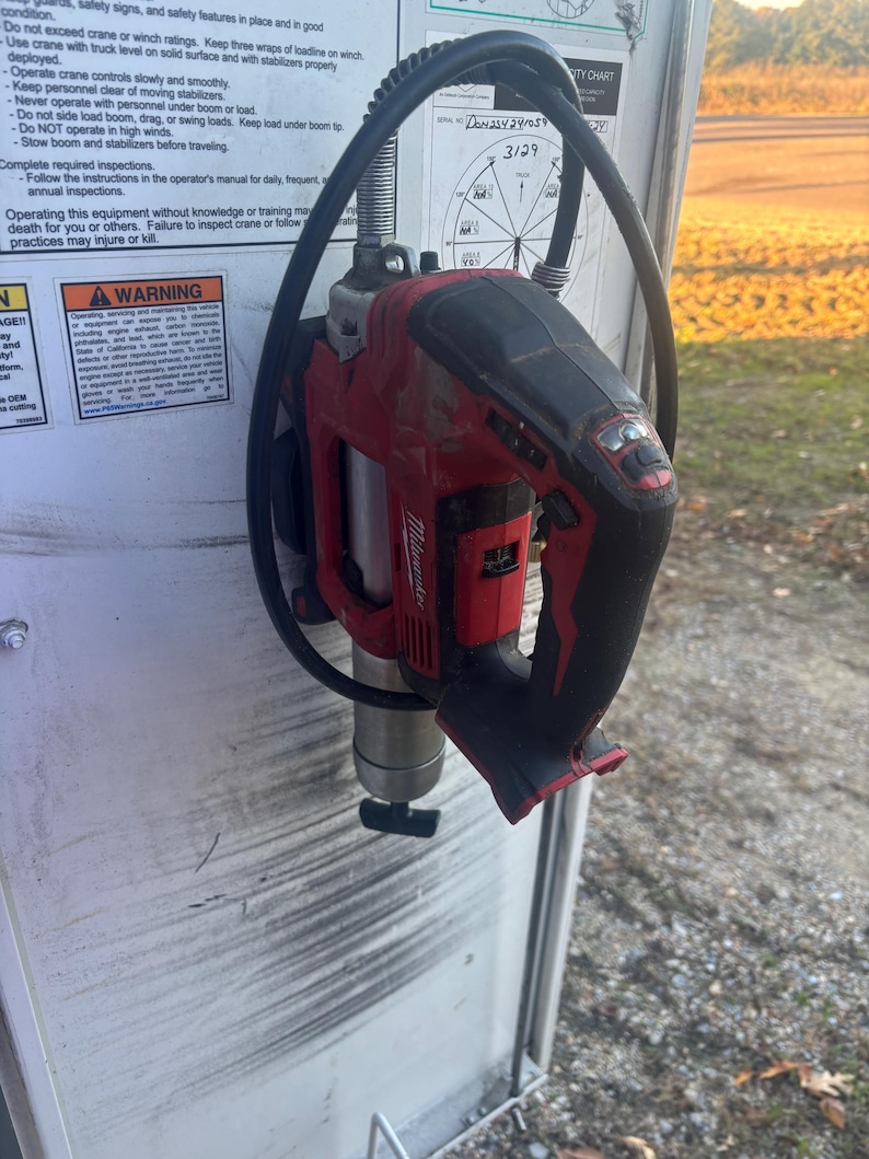 Może przedstawiać: Czerwono-czarne narzędzie elektryczne Milwaukee, prawdopodobnie wiertarka lub zakrętarka udarowa, jest zamontowane na białej powierzchni. Narzędzie ma czarny uchwyt i srebrny osprzęt. Czarny kabel jest owinięty wok&oacute;ł narzędzia.