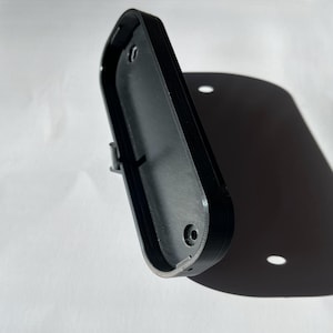 Puede incluir: Caja de plástico negro con dos agujeros para tornillos y un pestillo en el lateral.