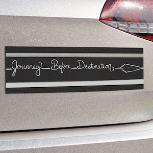 Könnte beinhalten: Ein rechteckiger schwarzer Autoaufkleber mit dem Text "Journey Before Destination" in weißer Schrift. Der Aufkleber hat einen weißen Streifen über und unter dem Text sowie eine Pfeilgrafik. Er ist an der Rückseite eines silbernen Autos angebracht.