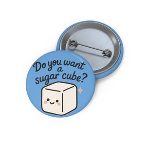 May include: A light blue button with the text "Do you want a sugar cube?" and a smiling sugar cube illustration. The button has a metal pin back.