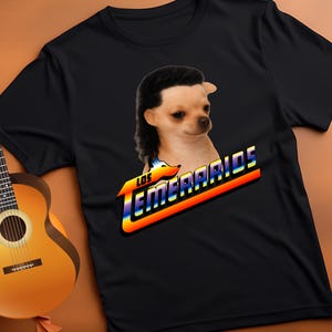 Puede incluir: Camiseta negra con un chihuahua con corte de pelo mullet. El texto "LOS TEMERARIOS" se muestra en una fuente retro con colores arcoíris. La camiseta está hecha de un material suave.