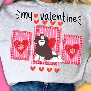 Puede incluir: Sudadera gris claro con un diseño gráfico que presenta un perro Shih Tzu, corazones y el texto "my Valentine". El diseño incluye elementos rosas y rojos, perfecto para el Día de San Valentín.