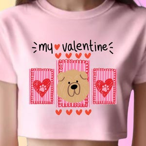 Puede incluir: Top corto rosa con un diseño de San Valentín. El gráfico incluye el texto "my valentine" encima de la cara de un perro y dos corazones con huellas de patas. El diseño está rodeado de corazones.