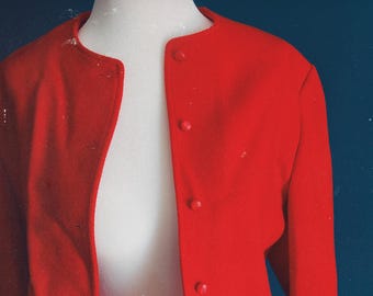 May include: A bright red jacket with a round collar and three matching buttons. The jacket is displayed on a white mannequin against a dark blue background. The jacket's fabric appears to be a smooth, possibly wool, material.