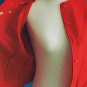 May include: A bright red jacket with a button-up front and two pockets. The jacket is displayed on a mannequin against a blue background. The inside of the jacket is visible, showing the lining and construction.
