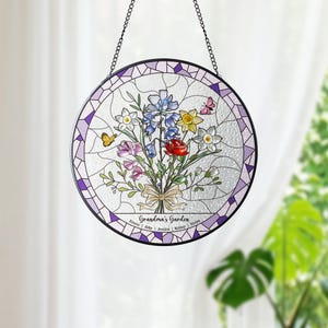 Puede incluir: Una vidriera redonda con un dise&ntilde;o de ramo floral. El ramo incluye rosas rojas, delfinios azules y narcisos amarillos, con mariposas. El texto "Grandma's Garden" est&aacute; en la parte inferior, con nombres.