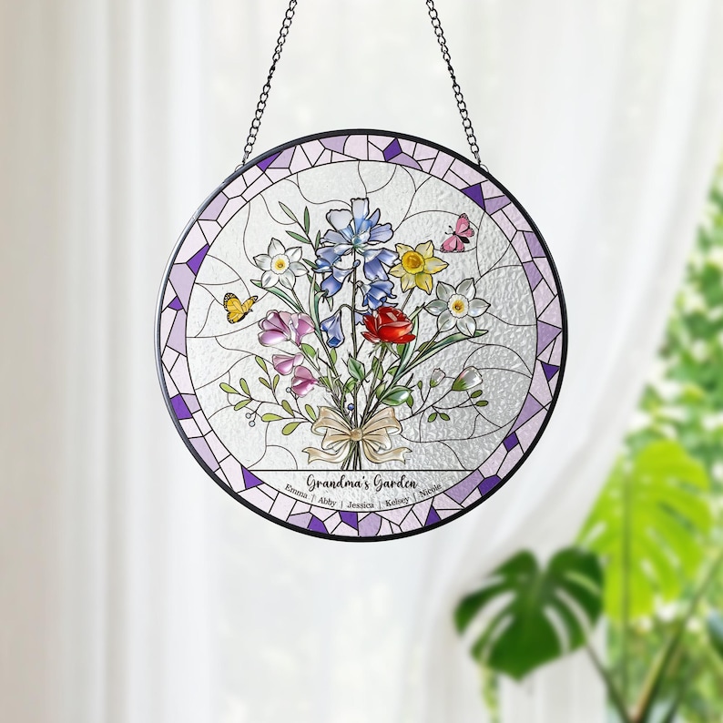 Puede incluir: Una vidriera redonda con un dise&ntilde;o de ramo floral. El ramo incluye rosas rojas, delfinios azules y narcisos amarillos, con mariposas. El texto "Grandma's Garden" est&aacute; en la parte inferior, con nombres.