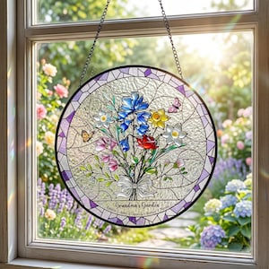May include: A round stained glass window hanging with a floral bouquet design. The bouquet features blue, red, yellow, and white flowers, with butterflies. The text "Grandma's Garden" is at the bottom, with names below. The window is framed in black and purple.