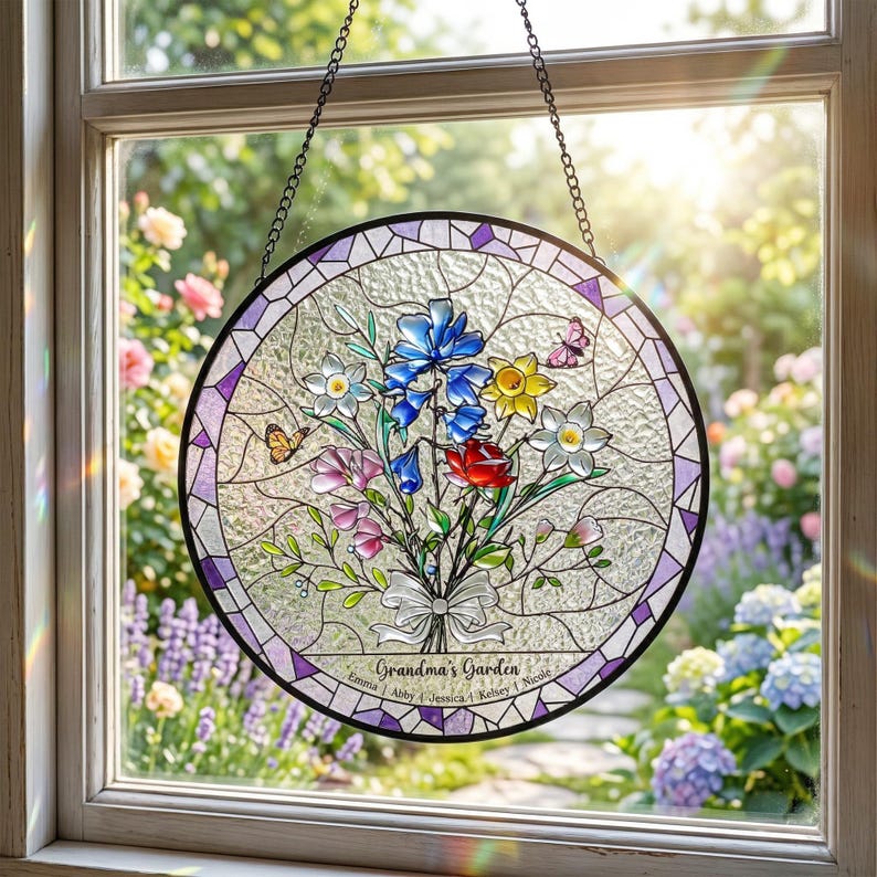 Puede incluir: Un colgante de ventana redondo de vidrieras con un dise&ntilde;o de ramo floral. El ramo presenta flores azules, rojas, amarillas y blancas, con mariposas. El texto "Grandma's Garden" est&aacute; en la parte inferior, con nombres debajo. La ventana est&aacute; enmarcada en negro y morado.