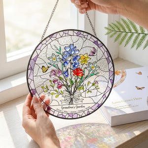 May include: A round stained glass window with a floral bouquet design. The bouquet features red, blue, yellow, and purple flowers, with butterflies. The text "Grandma's Garden" is displayed below the flowers, with names beneath. A chain is attached for hanging.