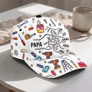Può includere: Un cappellino da baseball bianco con un motivo colorato di attrezzi da costruzione, tra cui chiavi inglesi, trapani e rulli per verniciare. Il design presenta un pugno centrale con il testo PAPA e i nomi KIM, LEO, EMMA, NOAH e MIA.