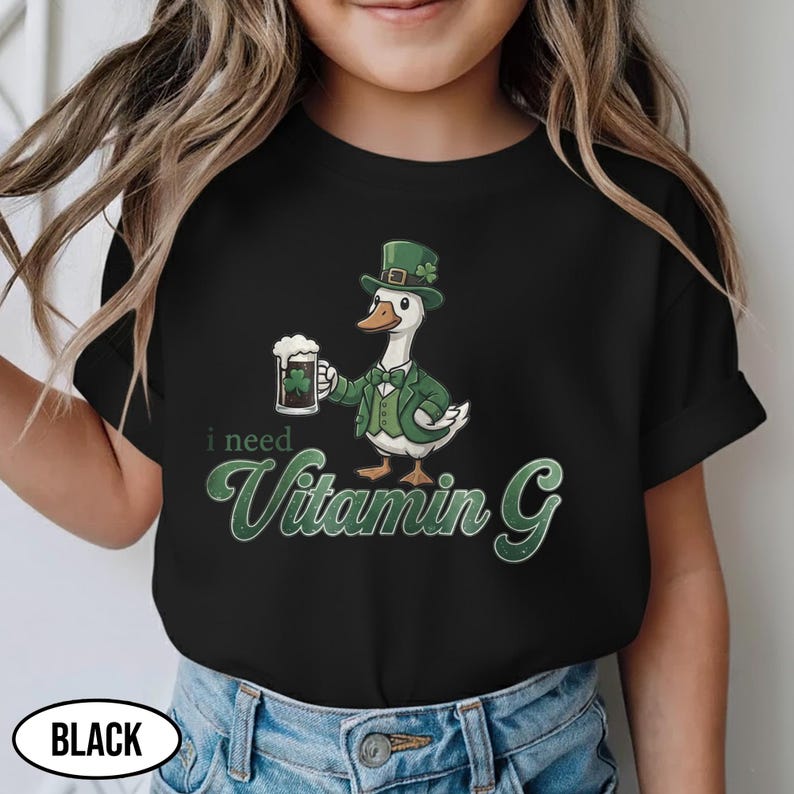 May include: Black t-shirt featuring a cartoon goose in a green suit and hat, holding a beer mug with a shamrock. The text "i need Vitamin G" is displayed in green. The word "BLACK" is in a white oval at the bottom.
