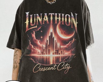 May include: Dark gray t-shirt featuring a futuristic cityscape design with the words "UNATHION" and "Crescent City" in a stylized font. The graphic includes a red and orange moon and a reflective water surface.