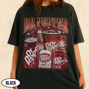 May include: Black t-shirt featuring a Dr Pepper design. The graphic includes the words "Dr Pepper" in a stylized font, along with images of soda cans, a bottle, and a cup of the beverage. The shirt is a dark color.