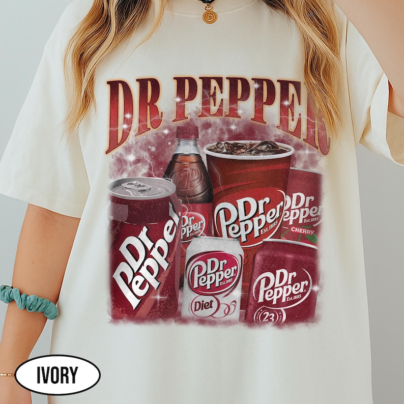 May include: Ivory-colored t-shirt featuring a Dr. Pepper graphic. The design includes images of Dr. Pepper cans, bottles, and a cup, with the brand name prominently displayed in a vintage style. The shirt is a casual wear item.