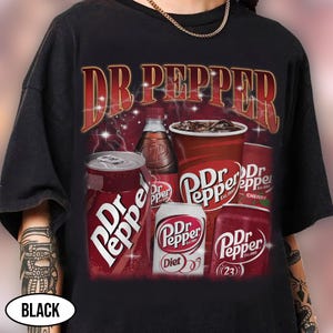 May include: Black t-shirt featuring a Dr Pepper graphic. The design includes various Dr Pepper products: cans, a bottle, and a cup, with the brand name in a vintage style. The shirt has a classic, retro aesthetic.