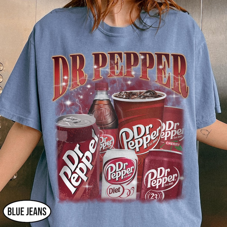 May include: A light blue t-shirt featuring a graphic of Dr Pepper products, including cans, a bottle, and a cup of soda. The Dr Pepper logo is prominently displayed in red and white. The text "DR PEPPER" is arched across the top.