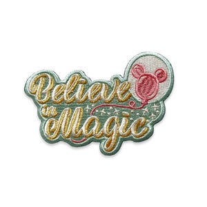 May include: Embroidered patch with the words "Believe in Magic" in gold script. The patch has a light green background with a pink Mickey Mouse head design on the right side. The patch is outlined in a light green color.