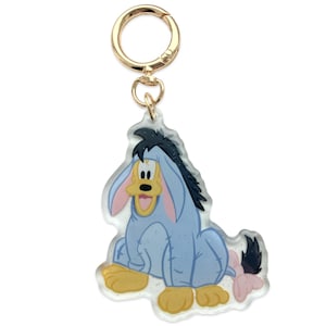 May include: A clear acrylic keychain featuring Eeyore from Winnie the Pooh. The keychain has a gold-colored clasp and a glittery finish. Eeyore is depicted in his classic blue, pink, and yellow colors.