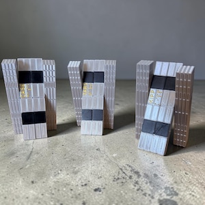 May include: Three gray and black geometric sculptures with the words "CASE", "TARS", and "KIPP" printed in gold. The sculptures are made of rectangular blocks and stand on a concrete surface.