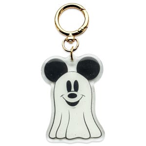May include: A clear acrylic keychain featuring a smiling ghost design in the shape of Mickey Mouse. The ghost has a white body with black ears and a black face. The keychain has a gold-colored clasp.