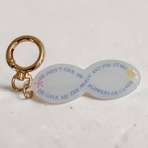May include: An infinity-shaped white keychain with a gold-toned metal lobster clasp. The text reads: HE DIDN'T GIVE ME THE MOON AND THE STARS, HE GAVE ME FLOWERS OR CANDY. It features a small pink starfish graphic and a tiny yellow seashell icon.