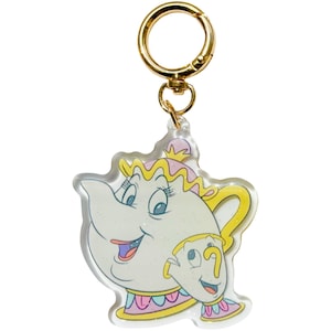 May include: A clear acrylic keychain featuring a cartoon teapot character with a gold-colored clasp. The teapot is white with pink, yellow, and blue accents. The keychain is a fun accessory.